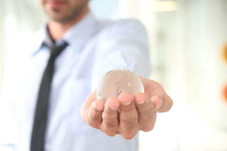 A man wearing a shirt and tie holds a clear sphere in his left hand