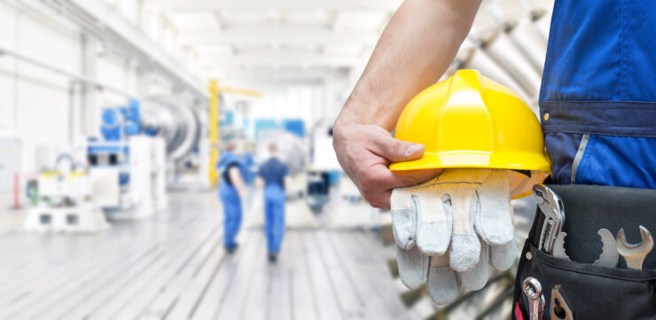 A worker holds their hard hat in gloves in a factory