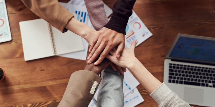 A group of hands put their hands into the centre of a circle on top of each other over work papers and a laptop