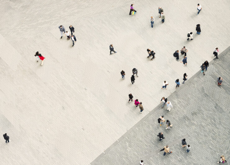 A bird's eye view of people walking across tiled concrete.