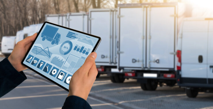 A tablet displaying data in front of a line of lorries and vans