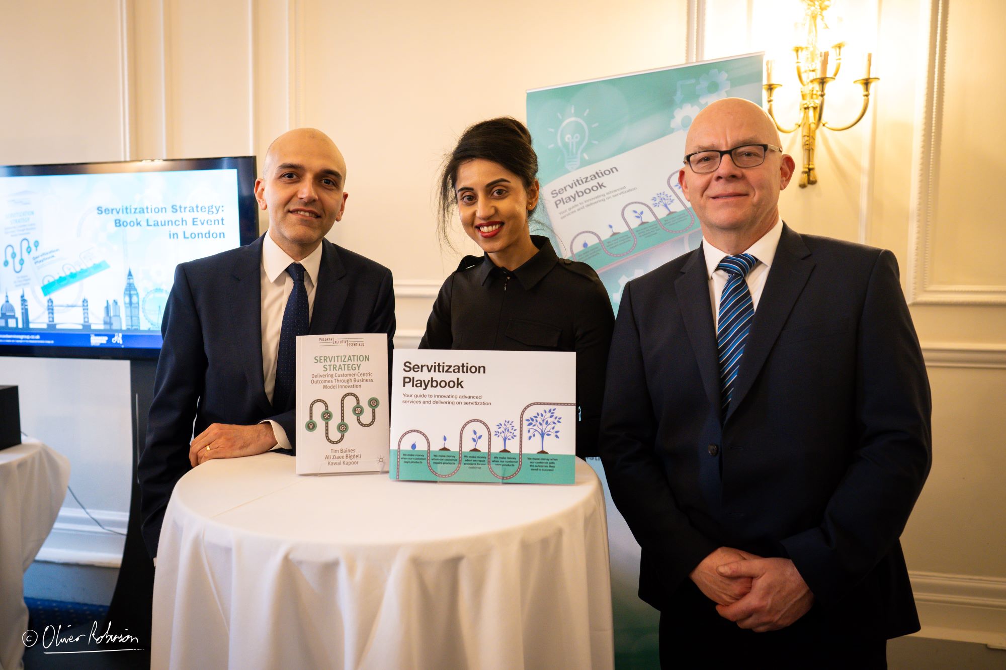Three ASG colleagues smile and pose by the Servitization Playbook at its launch event in London