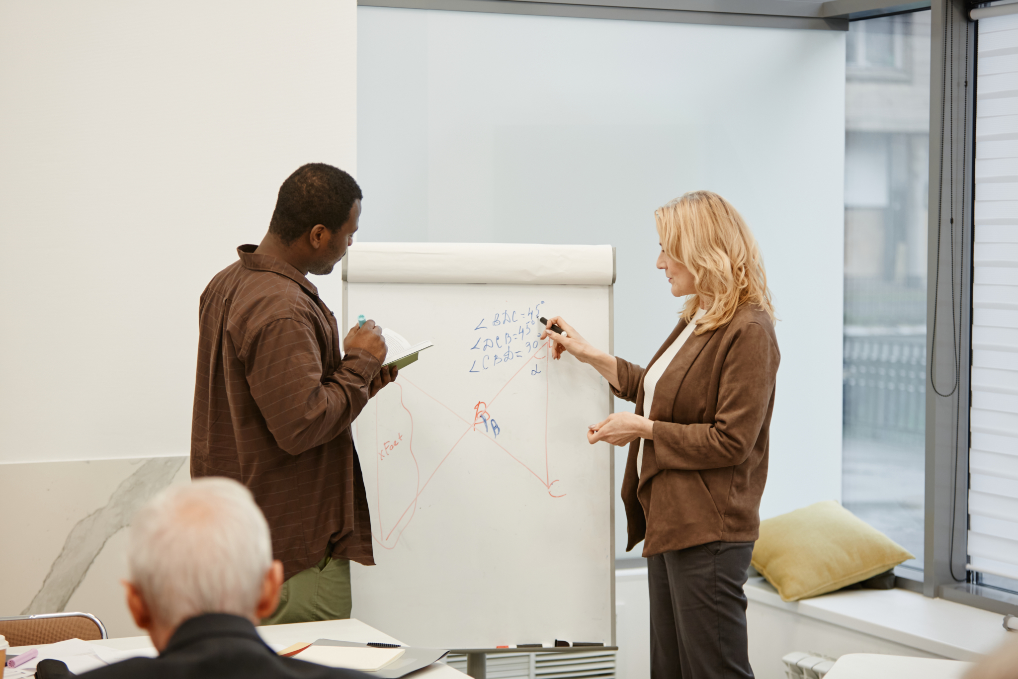 Two colleagues collaborate over equations on an A-board with paper and a marker